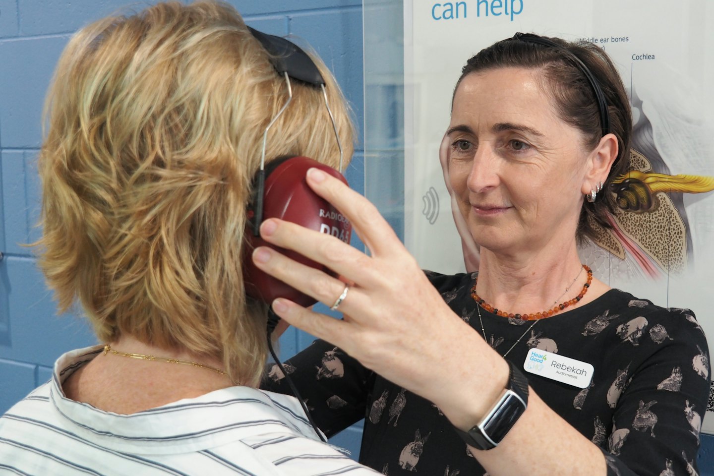 Audiologist adjusts red headphones on a patient during a hearing test.