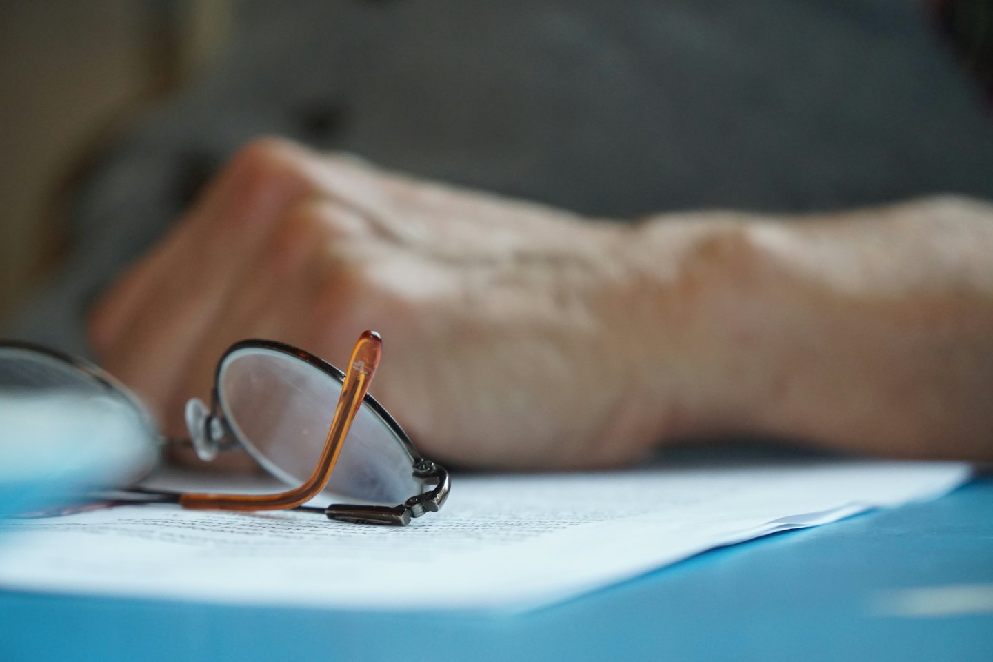 Reading glasses on white paper on a blue surface.